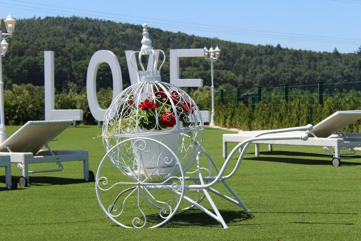 A white metal gazebo with a dome top, surrounded by white lounge chairs and a large 'LOVE' sign in the background.