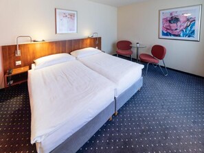 A hotel room with two beds, a desk, a chair, and a small table.