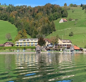 Un hotel frente al lago con varias construcciones, un muelle y un páramo boscoso al fondo.