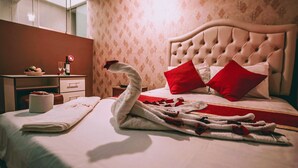 A neatly made bed with a swan-shaped towel, red pillows, and a fruit bowl on a bedside table. - Hostal Spring II (Huánuco)