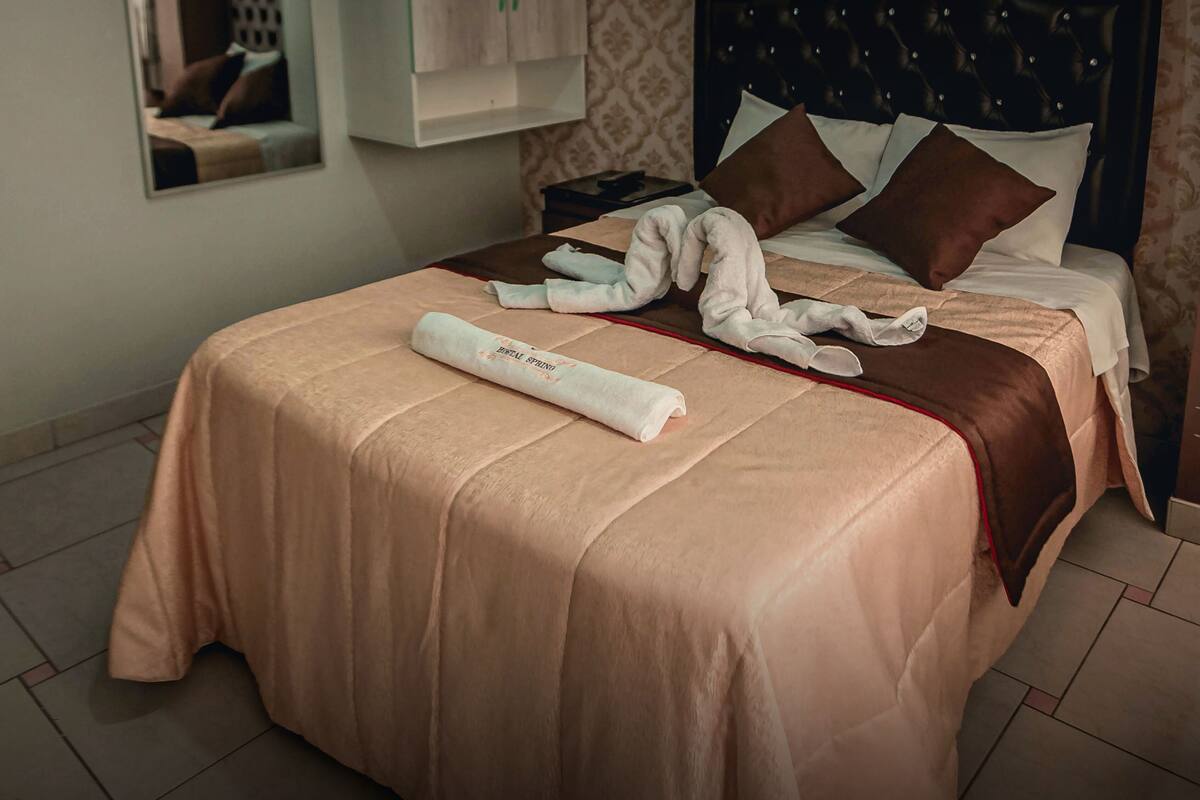 A neatly made bed with a beige bedspread, a rolled towel, and two pillows.
