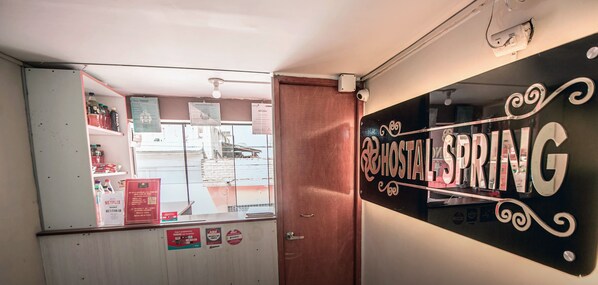 A room with a wooden door, a mirror reflecting a room with shelves and a sign that reads "HOSTAL ESPRING".
