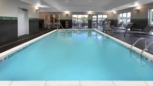 Una piscina interior con agua cristalina, marcas de profundidad de 5 metros y de longitud de 15 metros. Hay sillas de descanso y una mesa con sillas alrededor de la piscina.