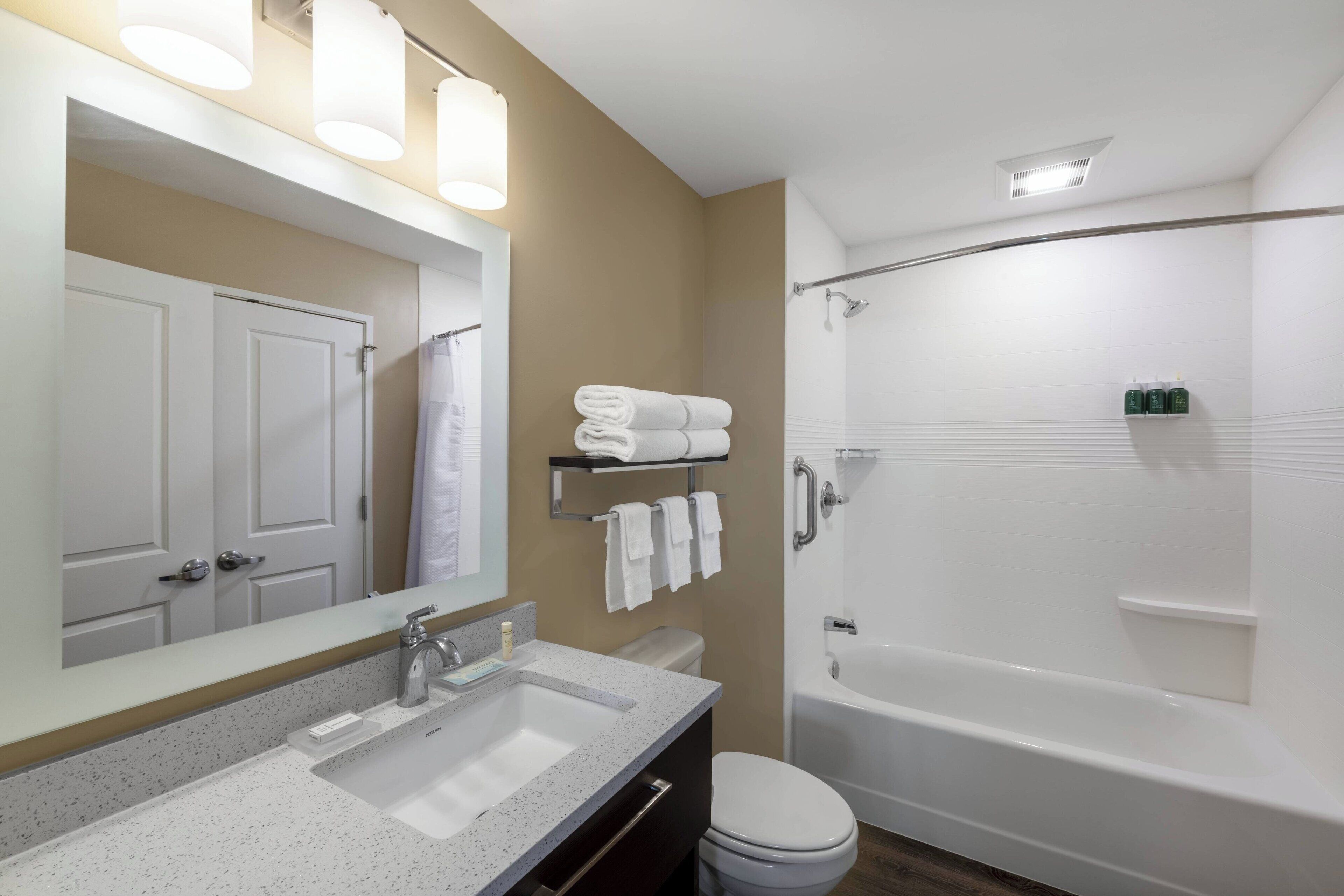 A modern bathroom with a sink, toilet, and bathtub. There are towels and toiletries on a shelf.