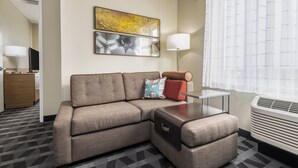 Una habitación de hotel moderna con un sofá seccional, una mesita, una lámpara y un ventanal con cortinas traslúcidas.
