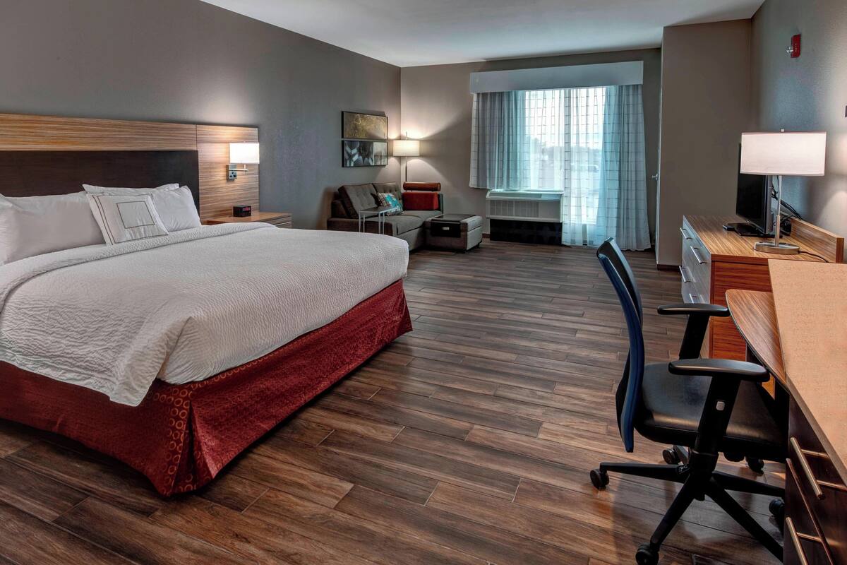 Une chambre d’hôtel avec un grand lit, un bureau avec une chaise, une petite table, un canapé et une fenêtre avec des rideaux.