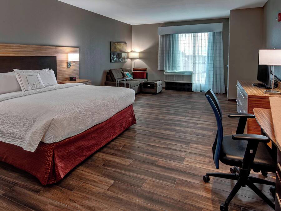 Habitación de hotel con una cama grande, un escritorio con una silla, una mesita, un sofá y una ventana con cortinas.