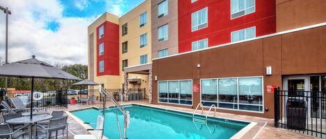 A hotel with a swimming pool, outdoor seating, and a clear sky.