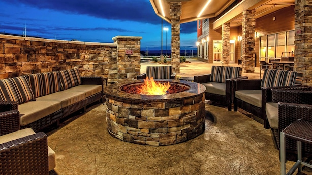 A stone fire pit surrounded by wicker furniture and a stone wall.