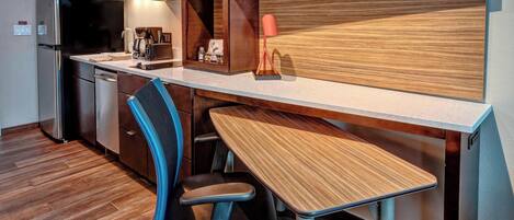 A compact kitchen with a microwave, coffee maker, and a sink. There is a wooden desk with a chair and a small lamp.