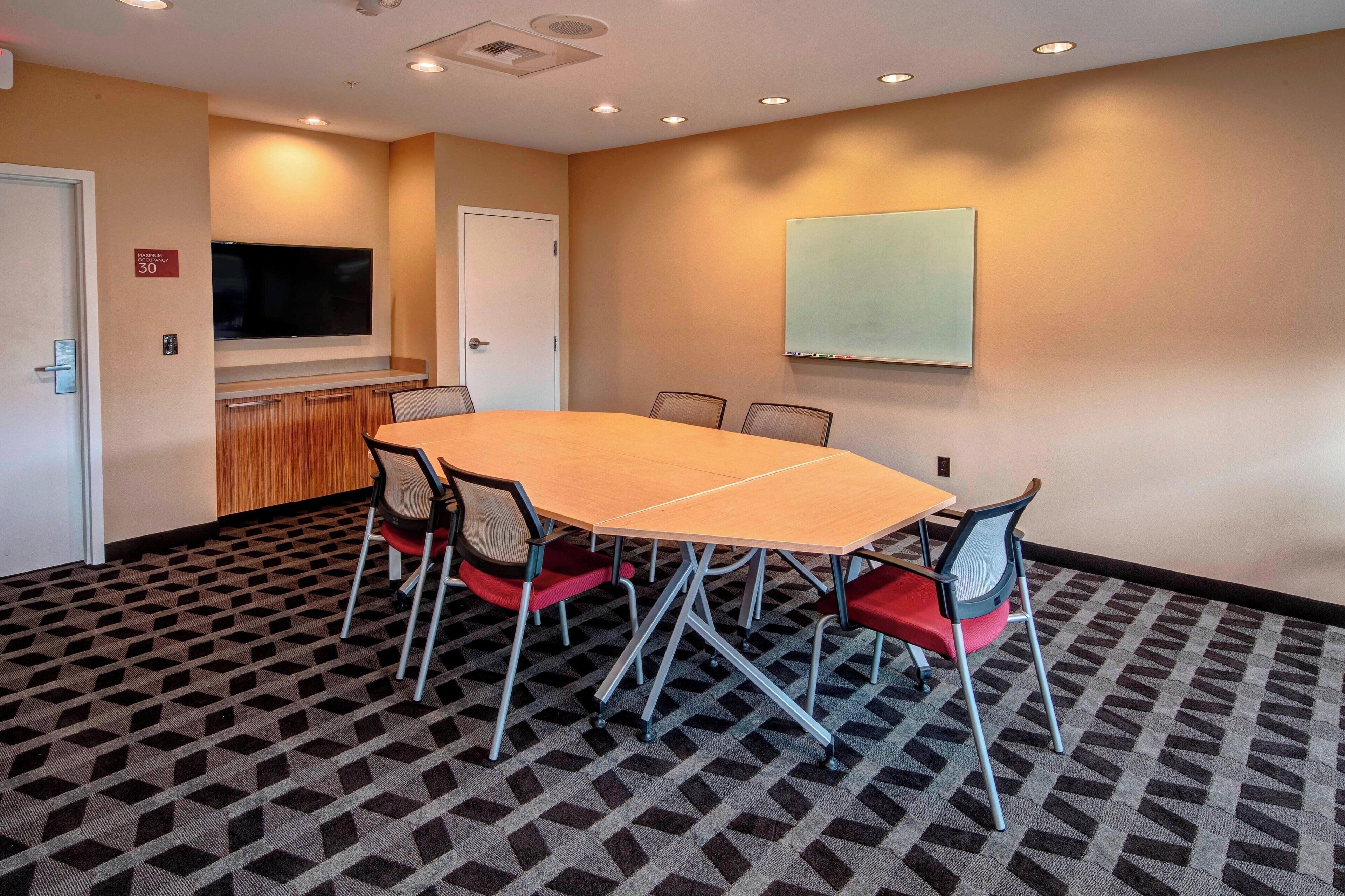 A conference room with a large table, chairs, a TV, and a whiteboard.