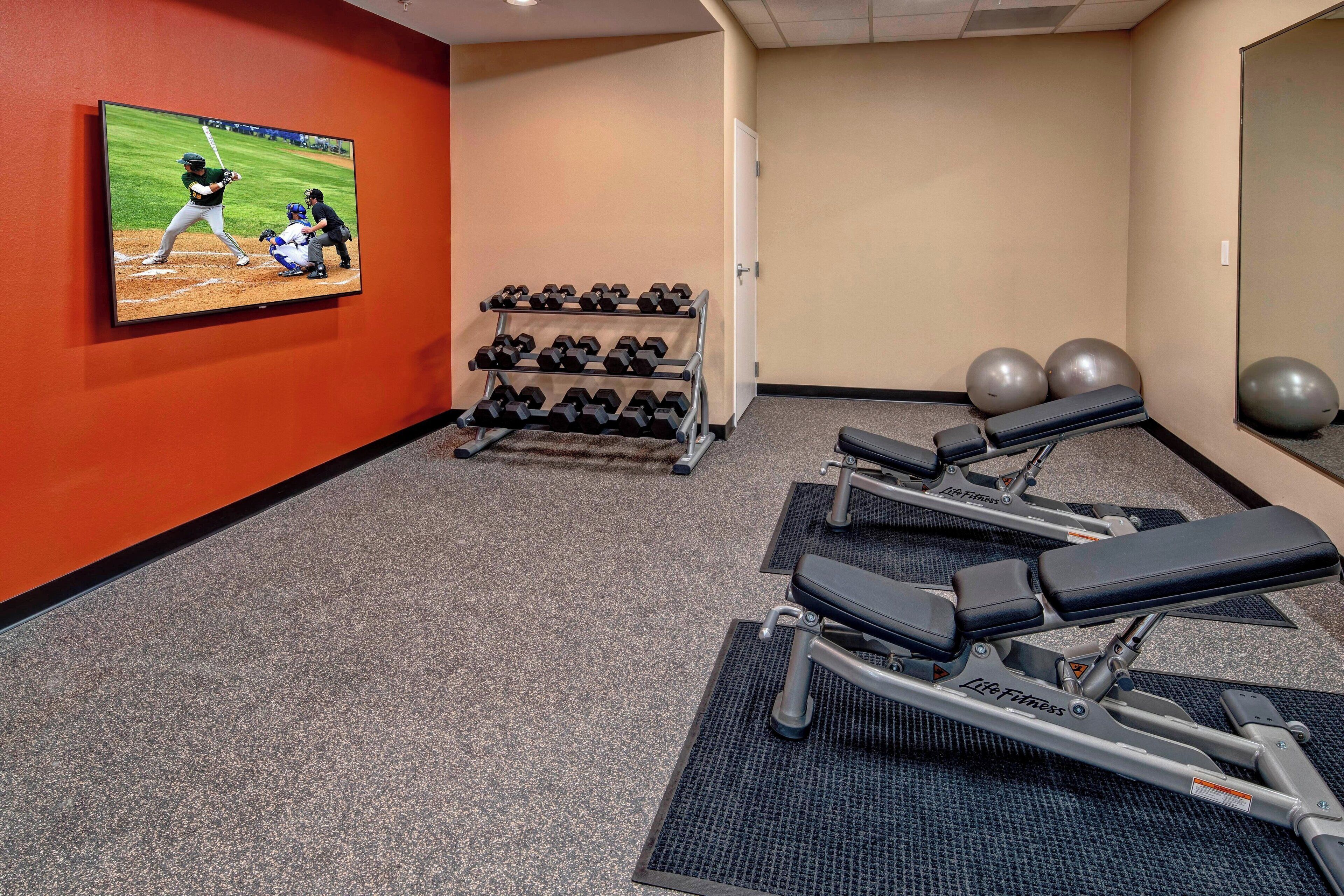 A gym with exercise equipment, a TV displaying a baseball game, and a mirror.