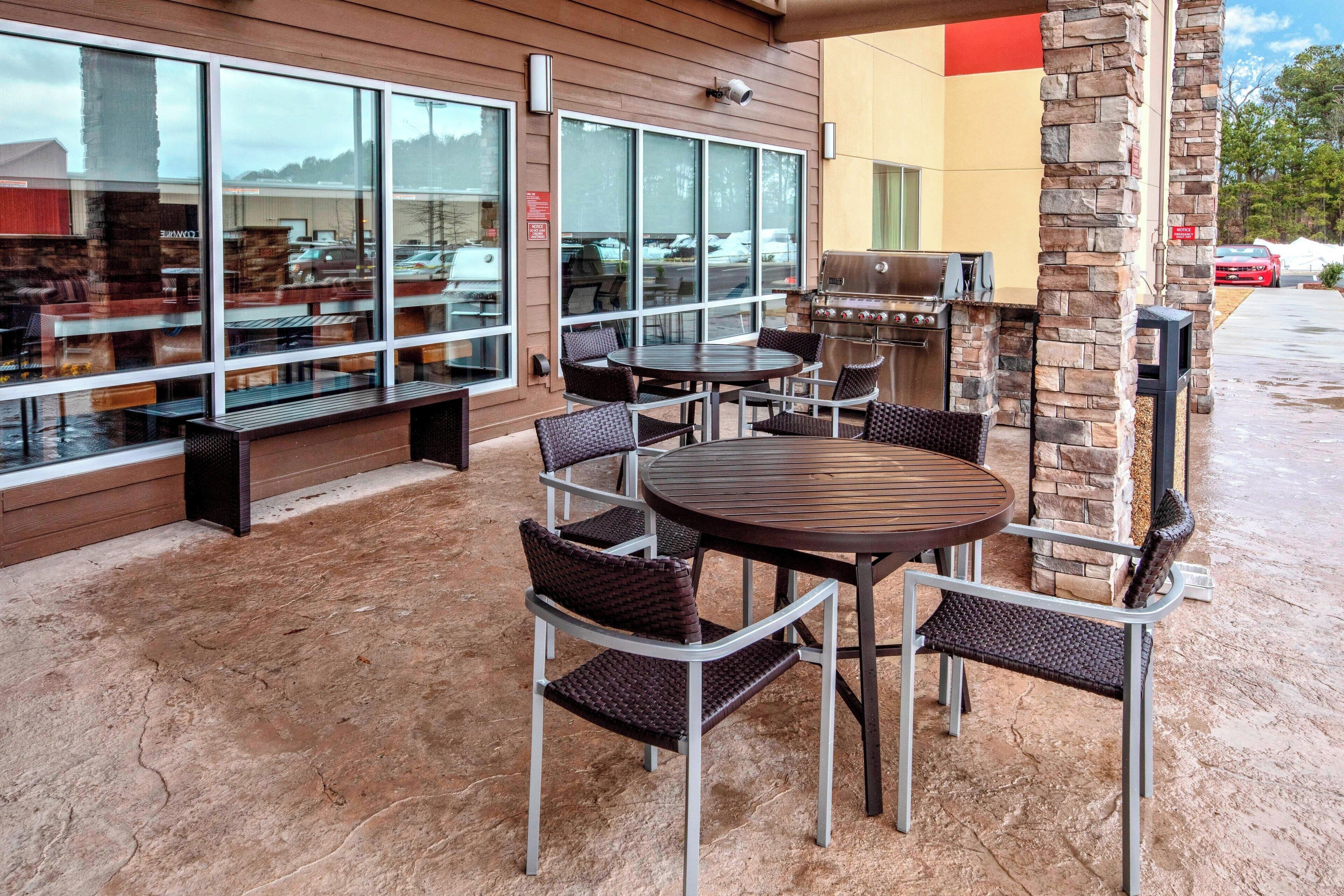 An outdoor patio with a round table and chairs, a grill, and a seating area with benches.