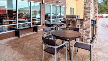 An outdoor patio with a round table and chairs, a grill, and a seating area with benches.