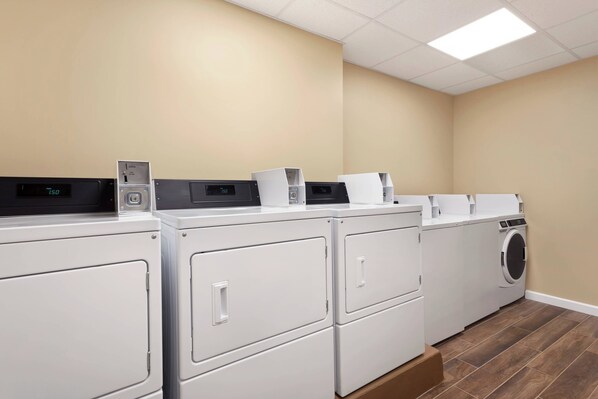 A laundry area with four washers and dryers, a control panel, and a digital display.