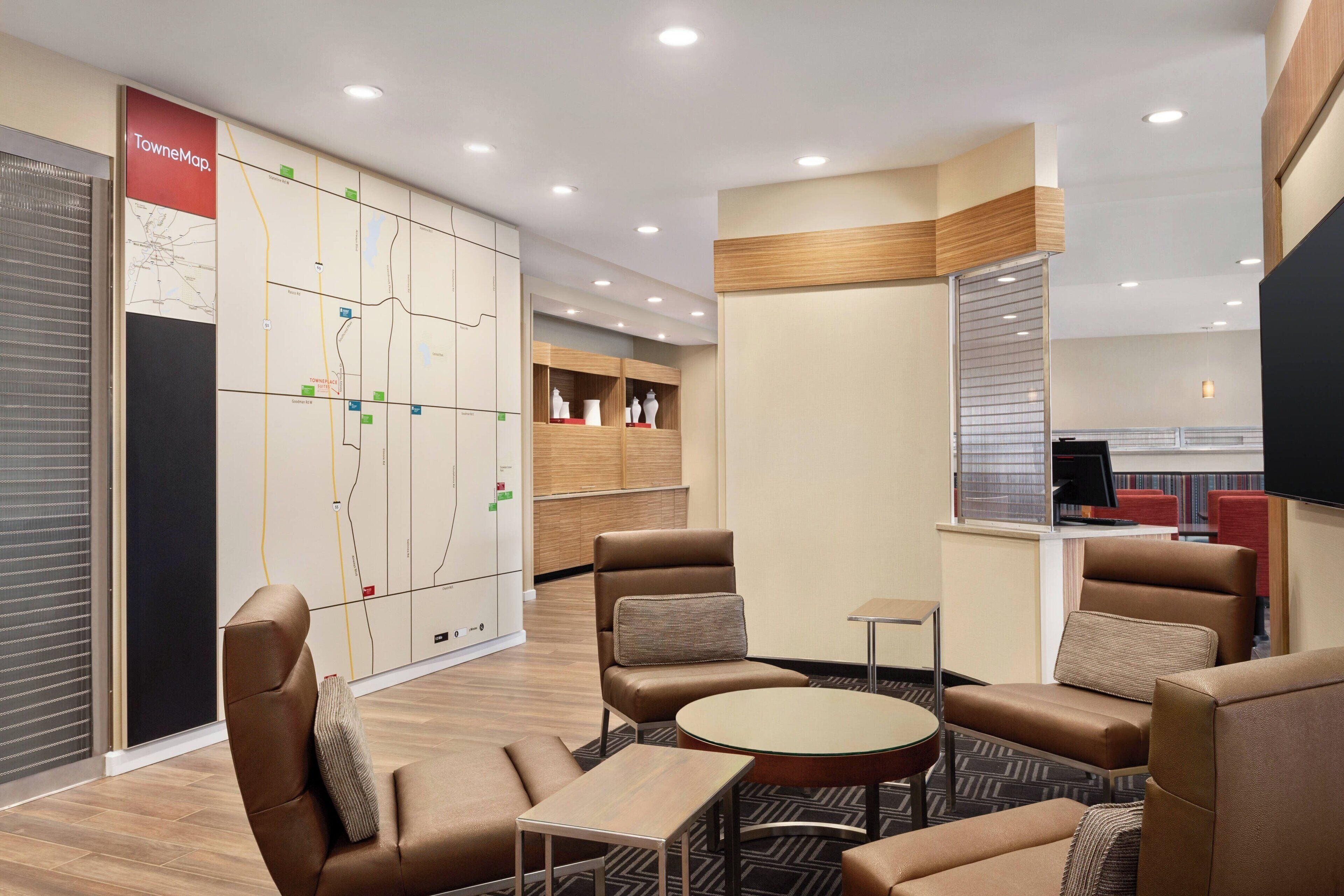 A modern hotel lobby with leather seating, a map wall, and a kitchenette area.