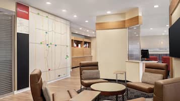 A modern hotel lobby with leather seating, a map wall, and a kitchenette area.