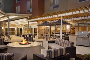 An outdoor patio with seating, a fire pit, and a grill area.
