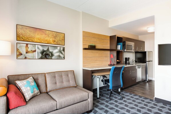 Une chambre d’hôtel moderne équipée d’un canapé, d’un bureau, d’une chaise et d’un coin cuisine avec un four à micro-ondes et un réfrigérateur.
