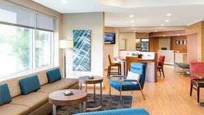 Un hall d’hôtel avec un canapé, des fauteuils, une petite table, un comptoir d’accueil et un écran de télévision.
