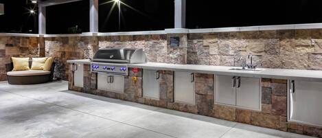 An outdoor kitchen area with a stone backsplash, built-in grill, and a seating area with cushions.