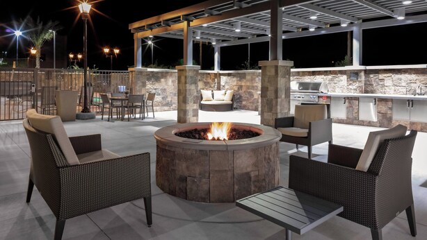 An outdoor patio area with a circular fire pit, wicker furniture, and a stone wall backdrop. - Residence Inn by Marriott Phoenix Mesa East (Mesa)