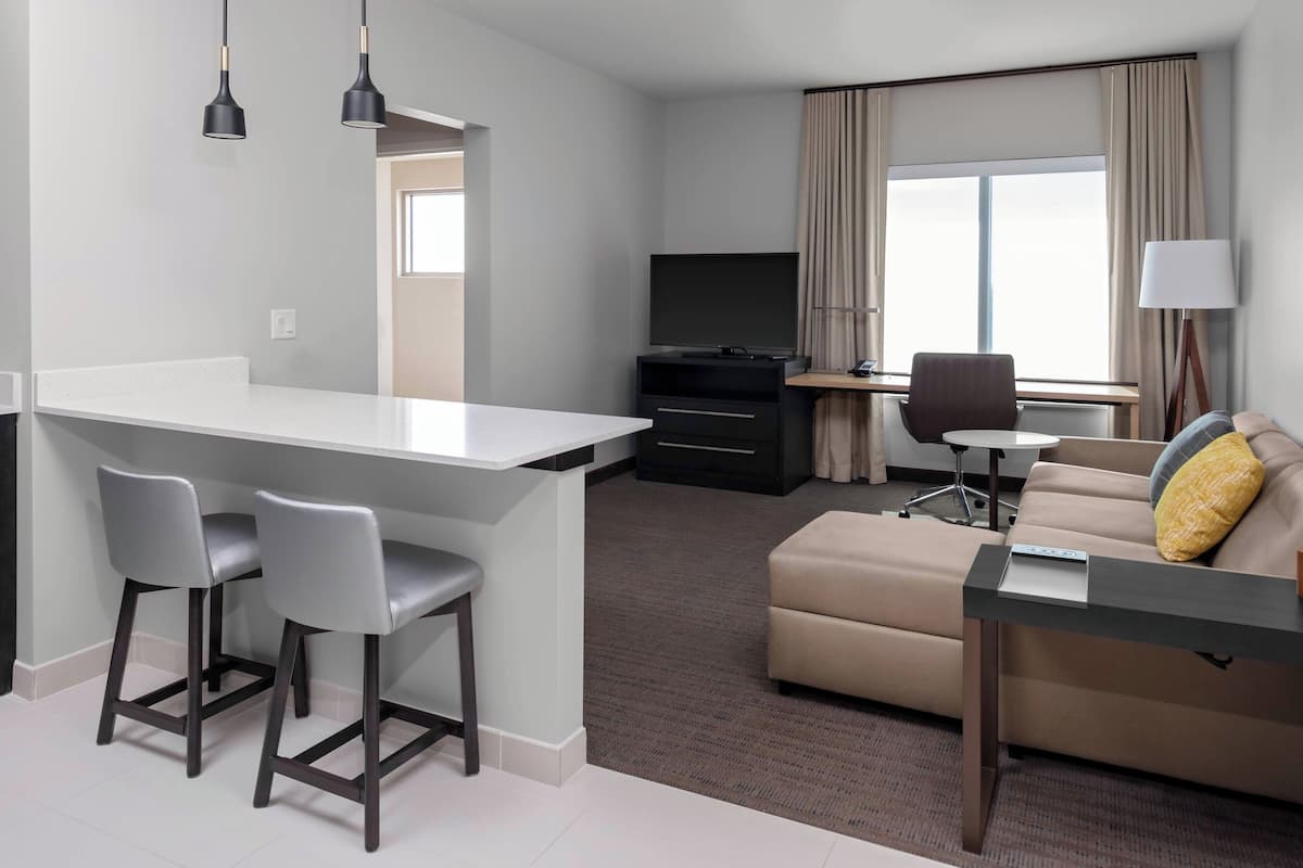 Ein modernes Hotelzimmer mit Küchenzeile, einer Sitzecke, einem Fernseher und einem Schreibtisch mit Stuhl.