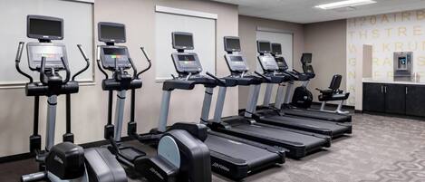 Ein Fitnessraum mit Laufbändern, Crosstrainern und einer Trinkbrunnen.
