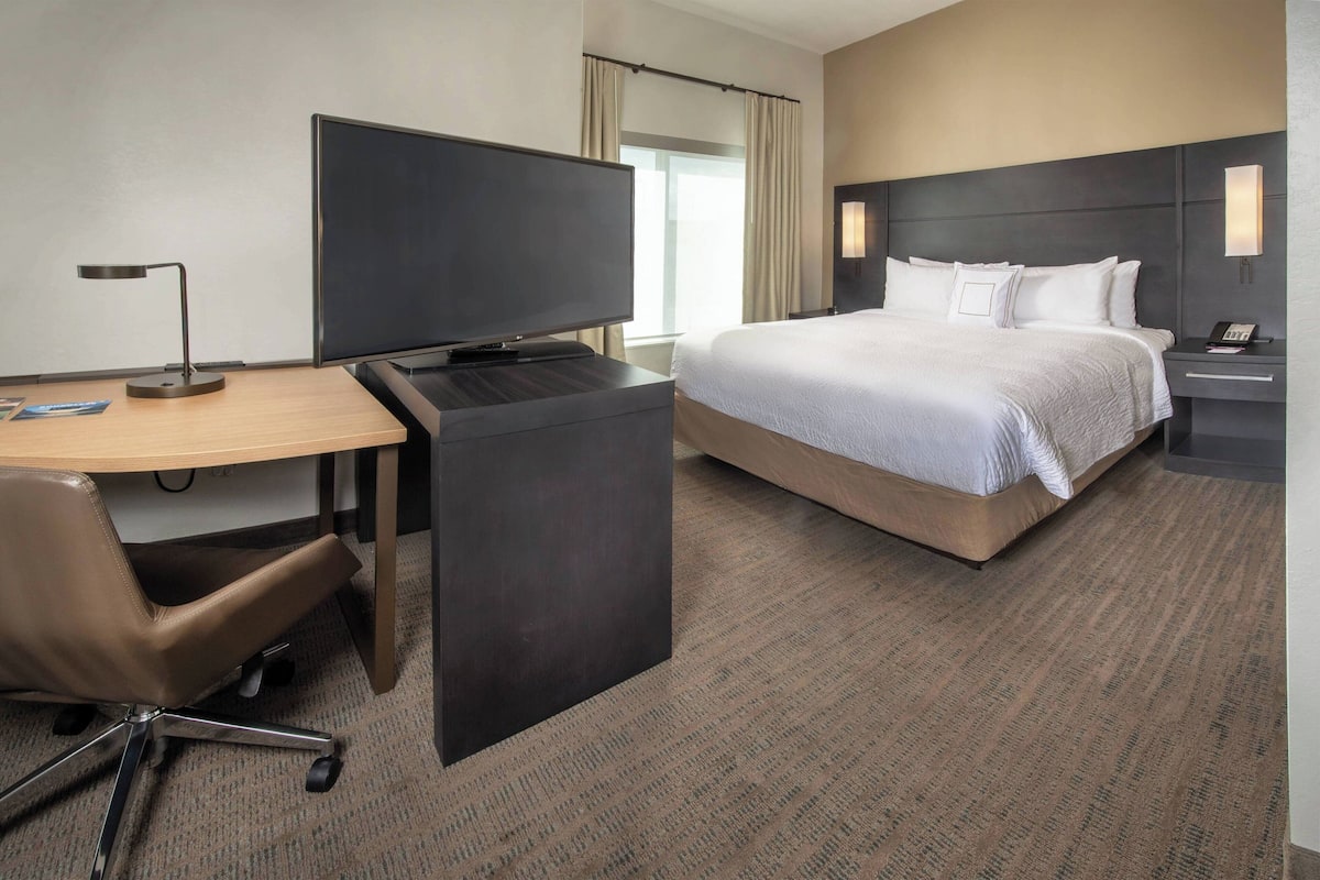 A hotel room with a bed, desk, chair, TV, and nightstand.