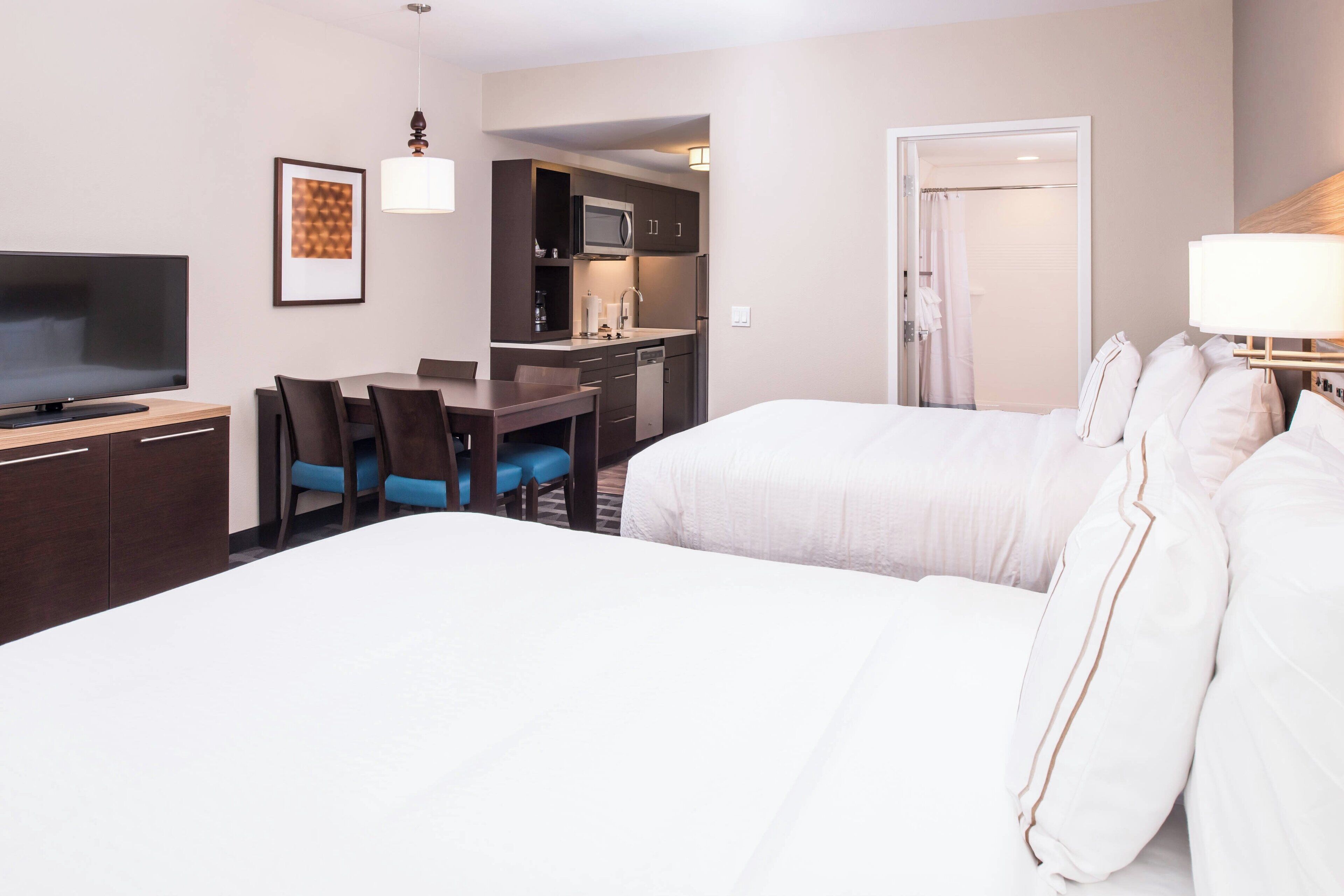A hotel room with a large bed, a desk with a chair, a television, a kitchenette, and a bathroom.