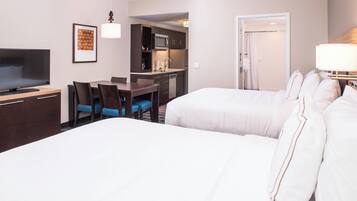 A hotel room with a large bed, a desk with a chair, a television, a kitchenette, and a bathroom.