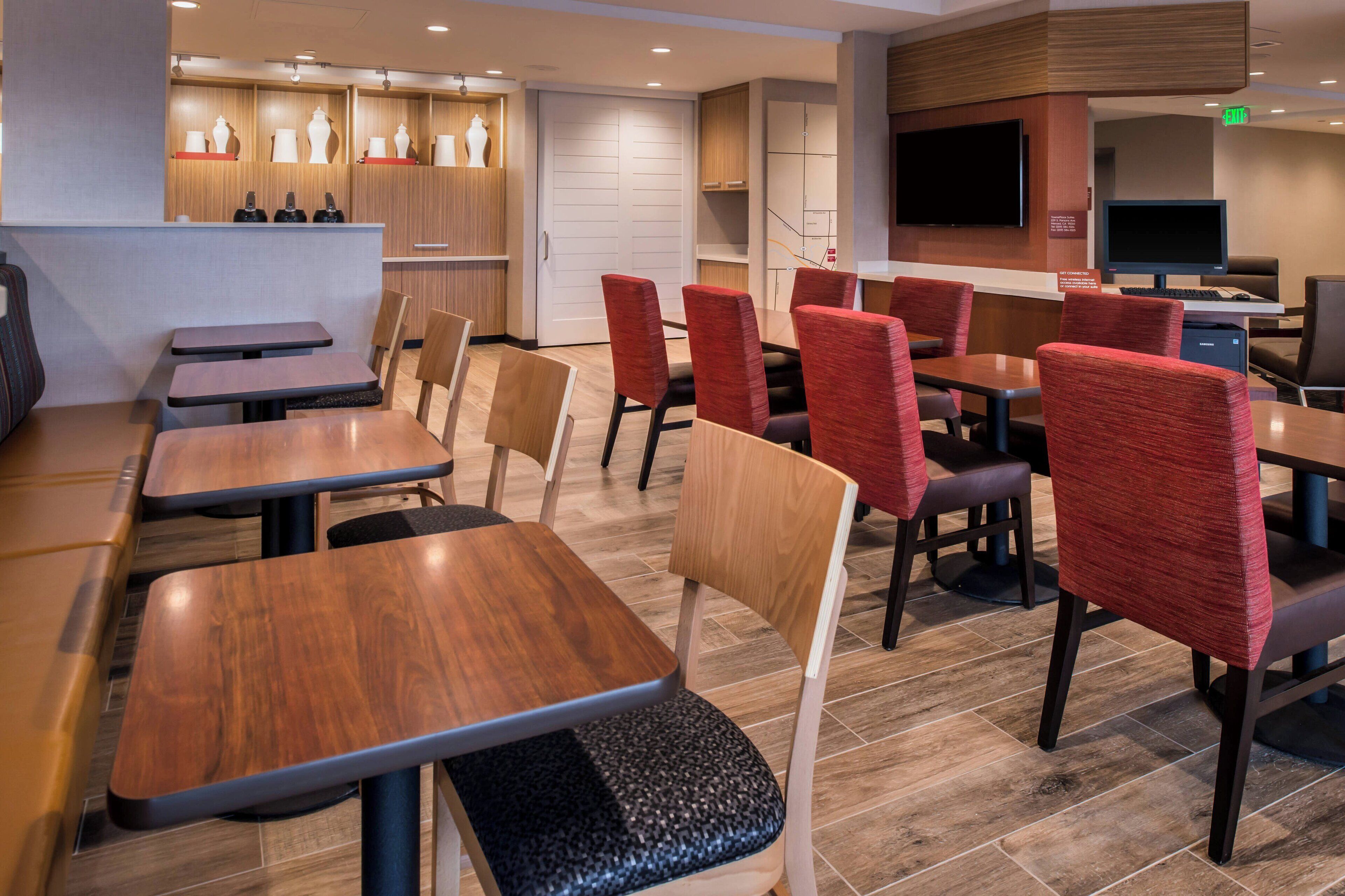 Een moderne hotel lobby met houten vloeren, meerdere zithoeken met tafels en stoelen, een televisie en een receptiebalie.