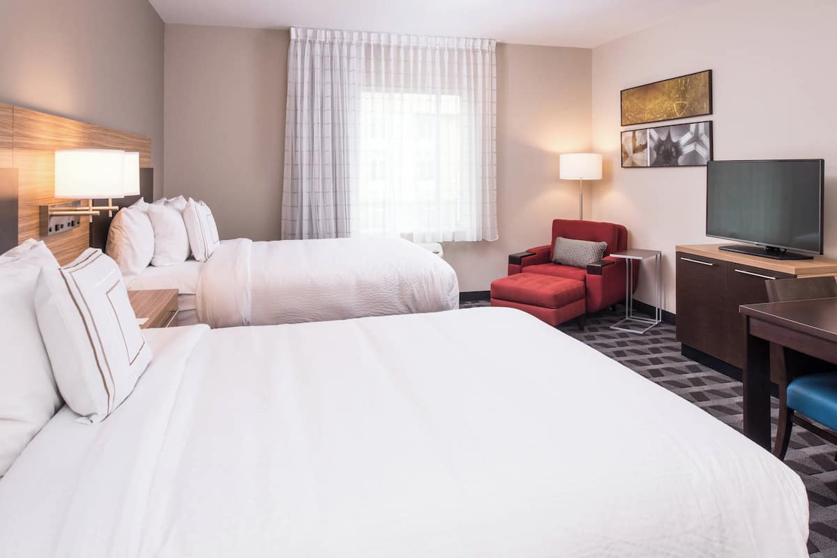 A hotel room with two beds, a red armchair, a TV, and a desk.