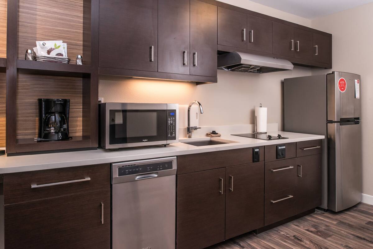 A modern kitchen with dark wood cabinets, stainless steel appliances, and a built-in dishwasher.