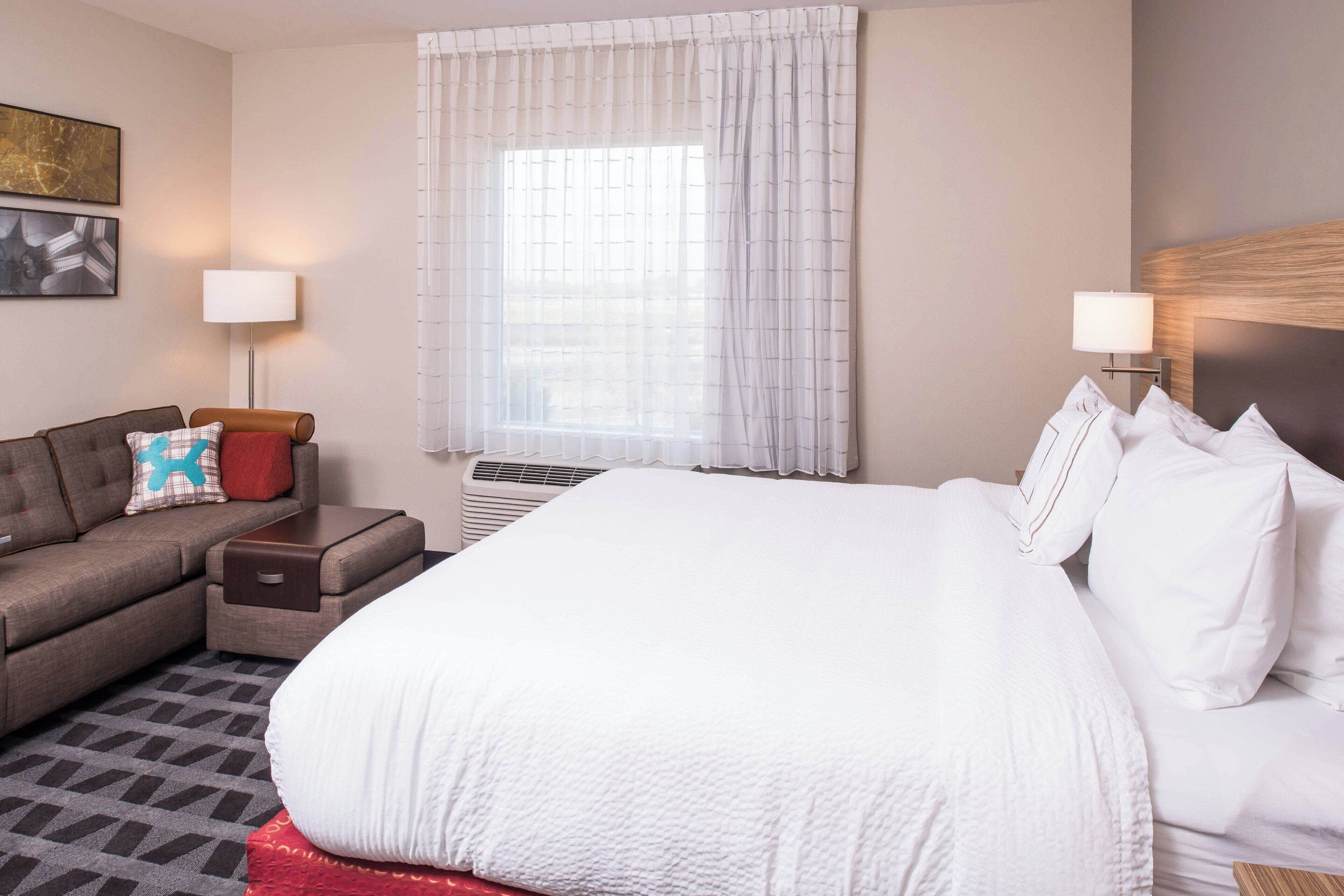 A hotel room with a large bed, a sofa, a small table, and a window with curtains.