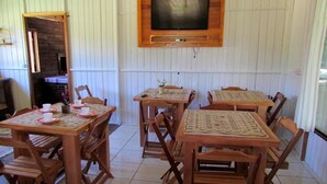 Un comedor con mesas y sillas de madera, un televisor montado en la pared y una chimenea de ladrillo al fondo.