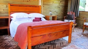 Una cama de madera con cabecera, una mesita de noche, una silla y una pequeña mesa con un florero.