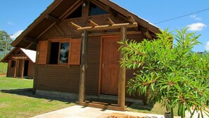 Una cabaña de madera con techo a dos aguas, un porche de madera y un pequeño jardín con una palmera.
