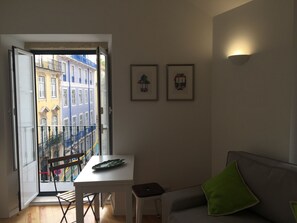 Ett rum med en balkong, ett bord, en stol, en soffa och två inramade tavlor på väggen.