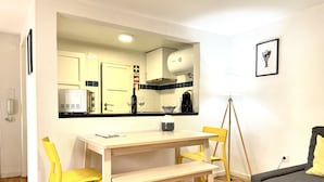 Un espace de vie compact comprenant un coin cuisine, un coin repas avec des chaises jaunes, un canapé gris et un tableau encadré au mur.