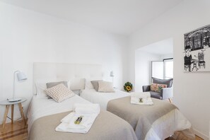Ett hotellrum med två sängar, ett litet bord med en lampa, en stol och ett konstverk som hänger på väggen.
