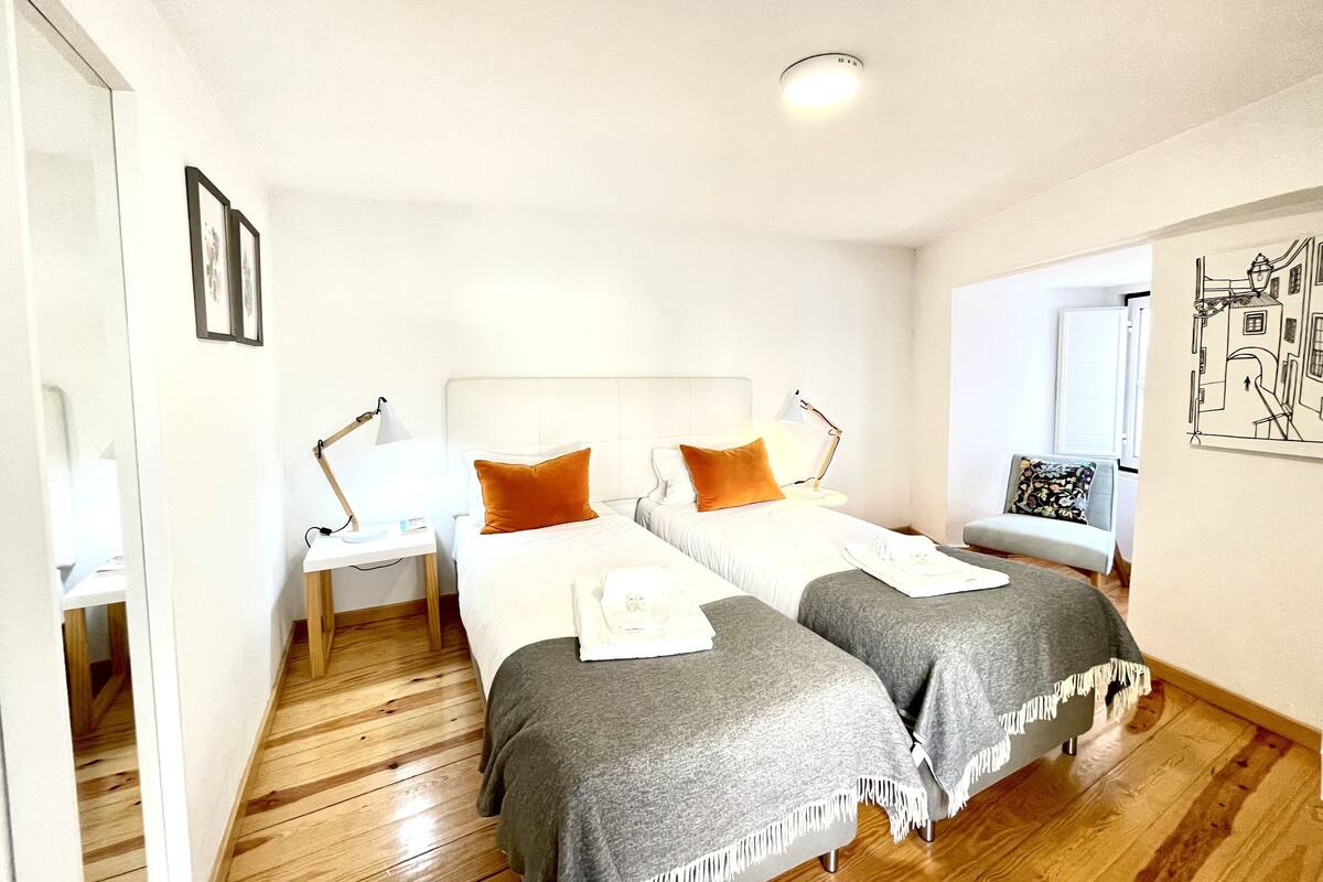 Ein Hotelzimmer mit zwei Betten, einem Nachttisch, einem Schreibtisch, einem Sessel und einem Wandbild.