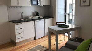 Une cuisine compacte avec des meubles blancs, un four à micro-ondes, un évier et un petit coin repas comprenant une table et une chaise.