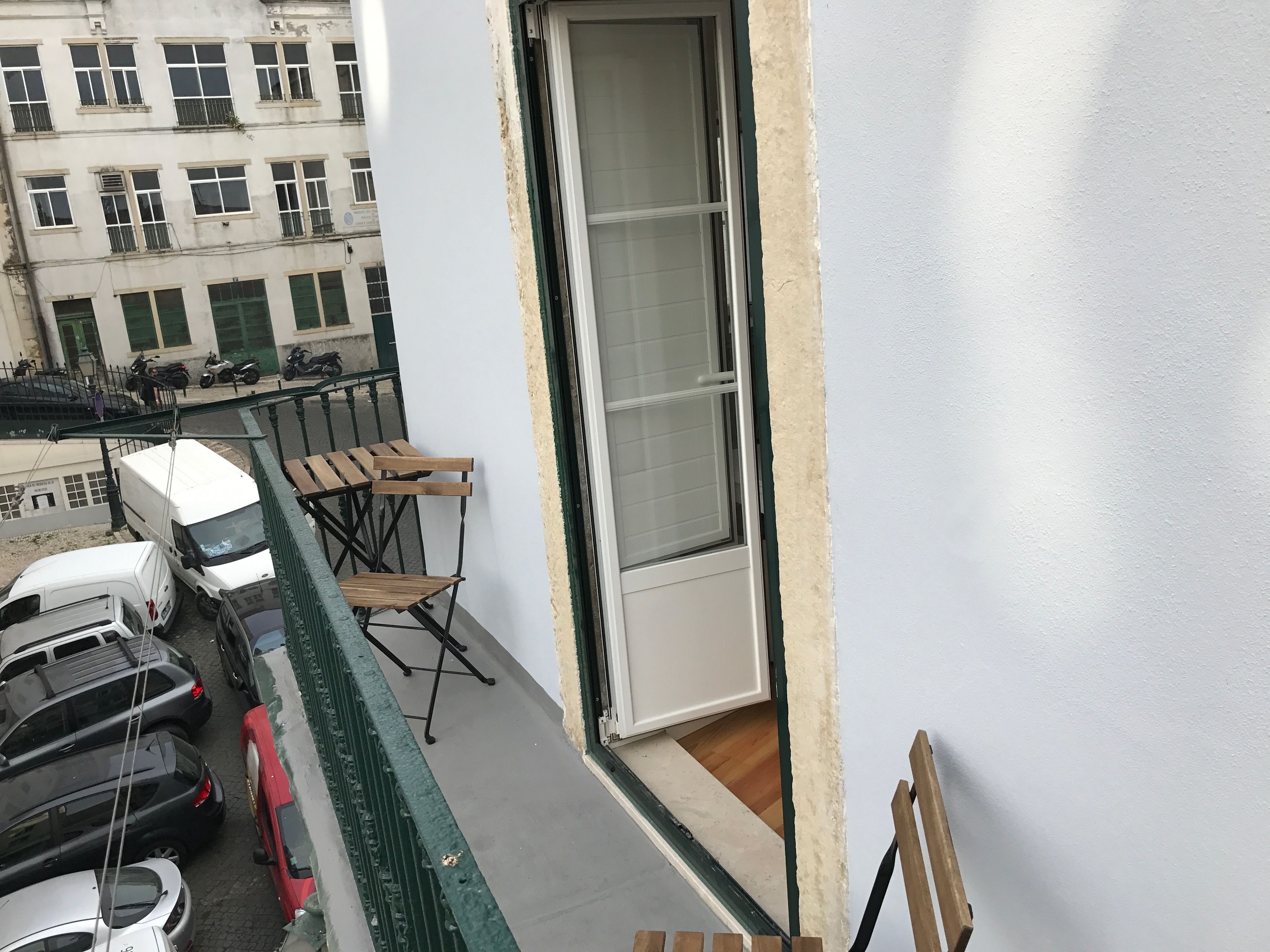 Un balcón con vista a coches estacionados y un edificio al fondo.