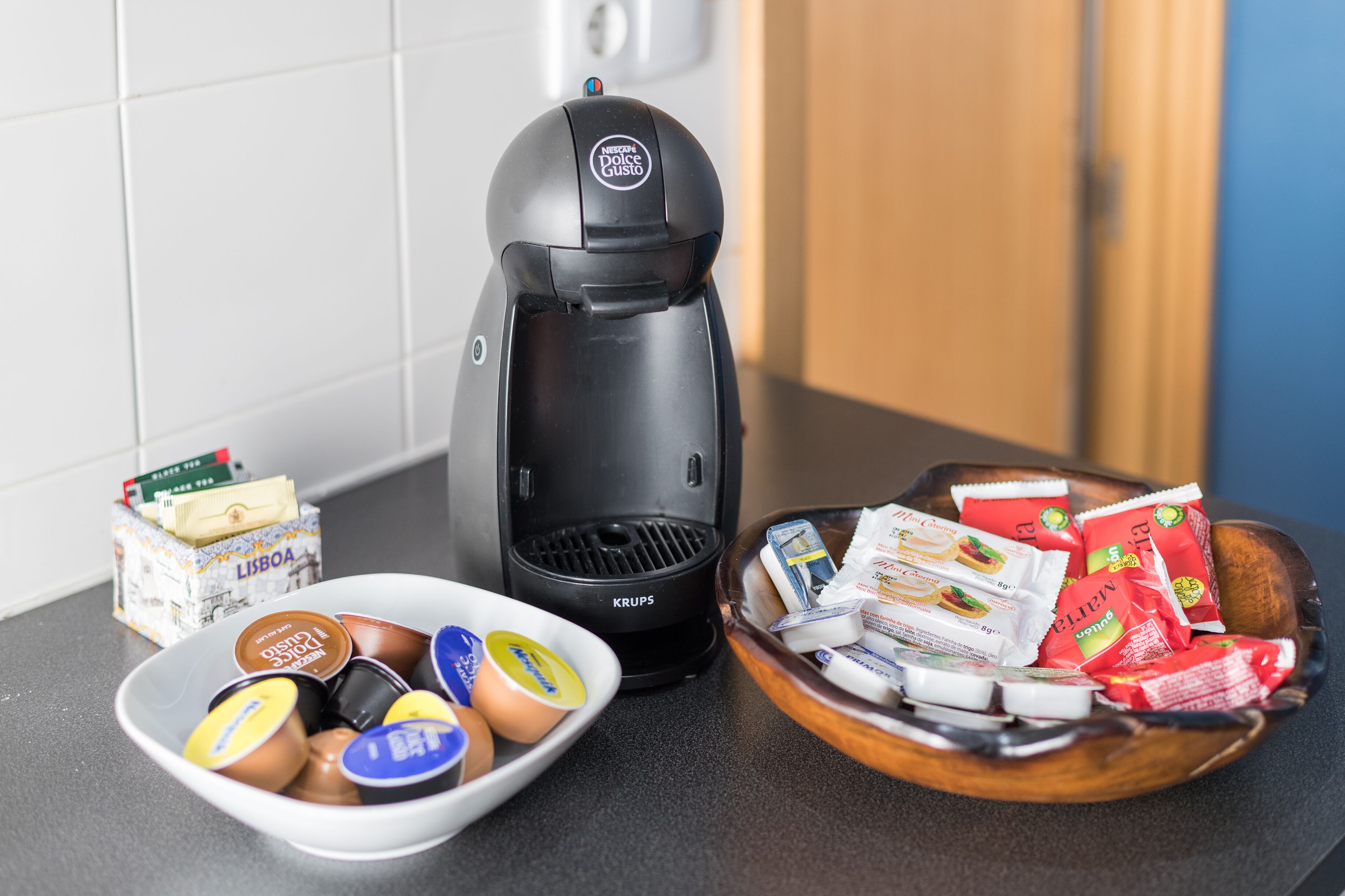 A coffee maker, a bowl of coffee pods, and a bowl of coffee packets on a kitchen counter.