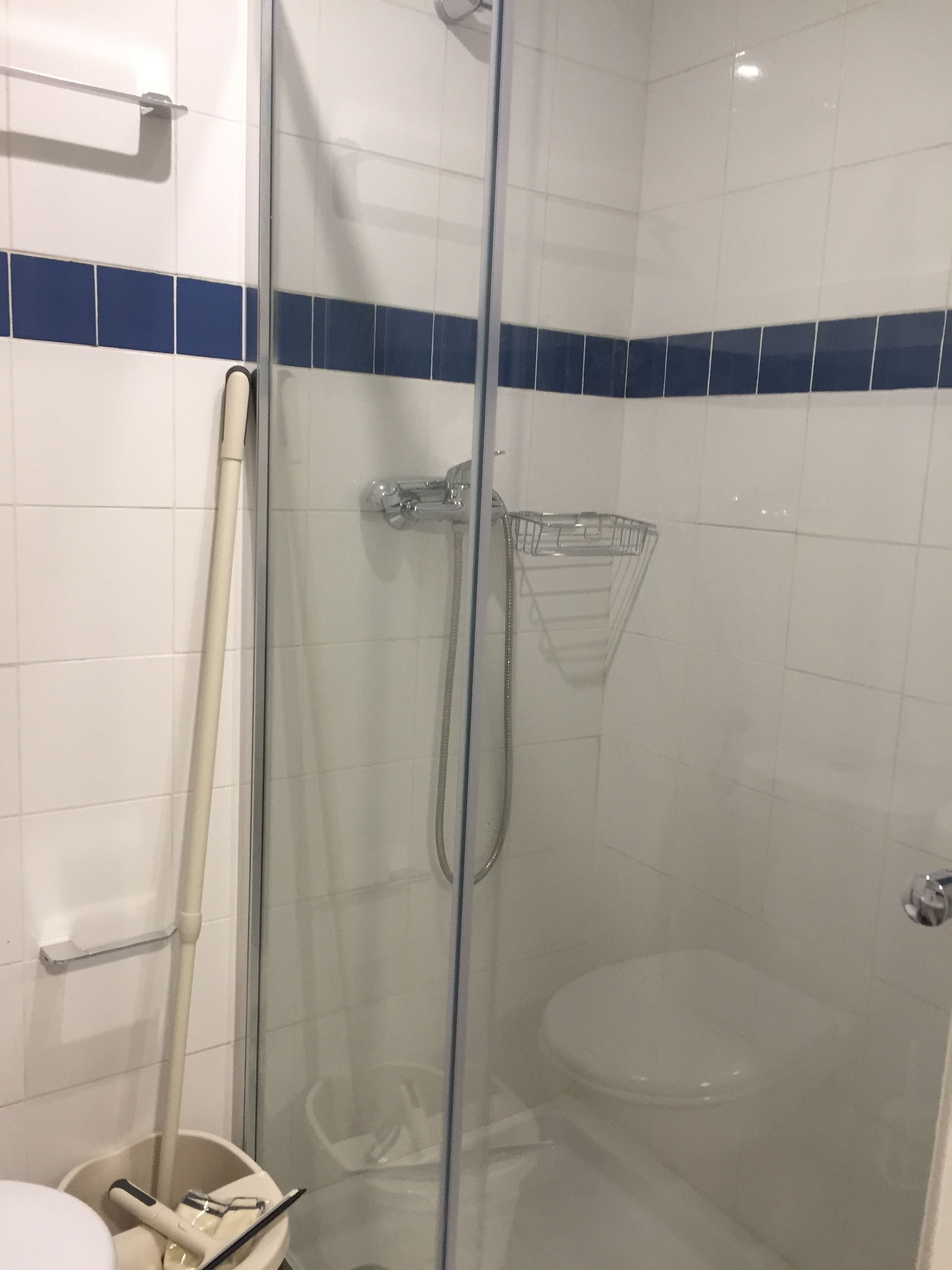 A glass-enclosed shower with a handheld showerhead and a wall-mounted faucet.