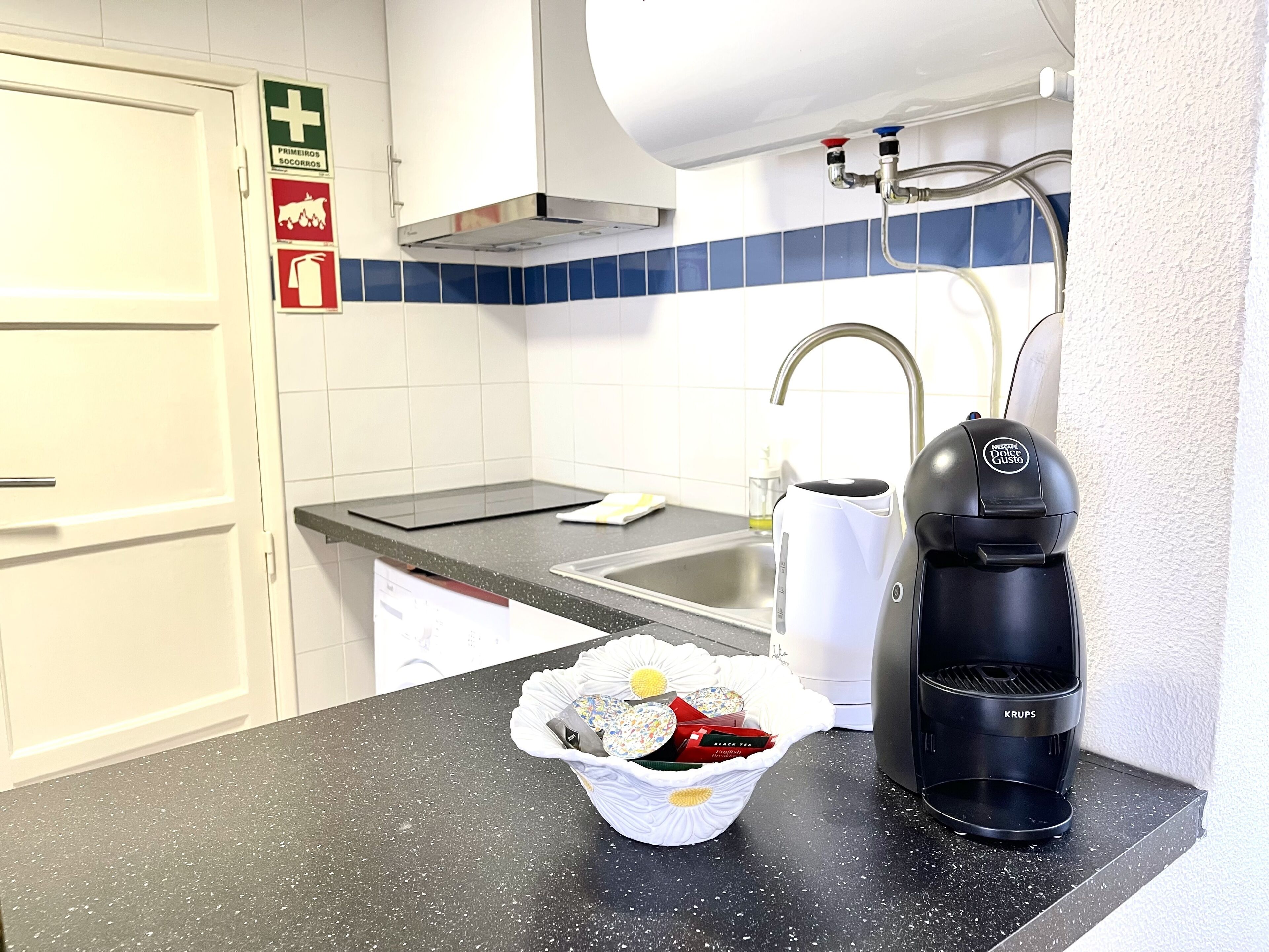 Une cuisine avec un plan de travail noir, une machine à café, un évier et une poubelle contenant des en-cas.