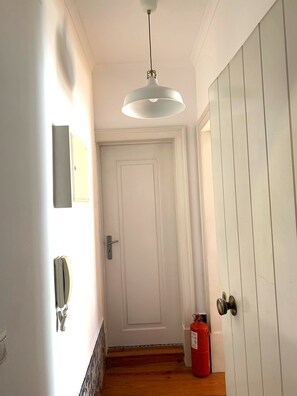 Un pasillo con una puerta blanca, un extintor y una lámpara colgante.