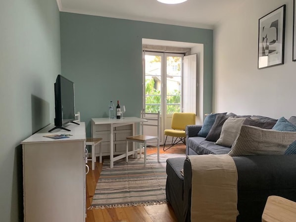 Una sala de estar con sofá, televisión, escritorio y una silla.