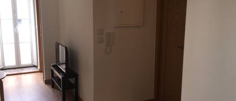 A hallway with a wooden floor, a door, a wall-mounted telephone, and a television on a stand.
